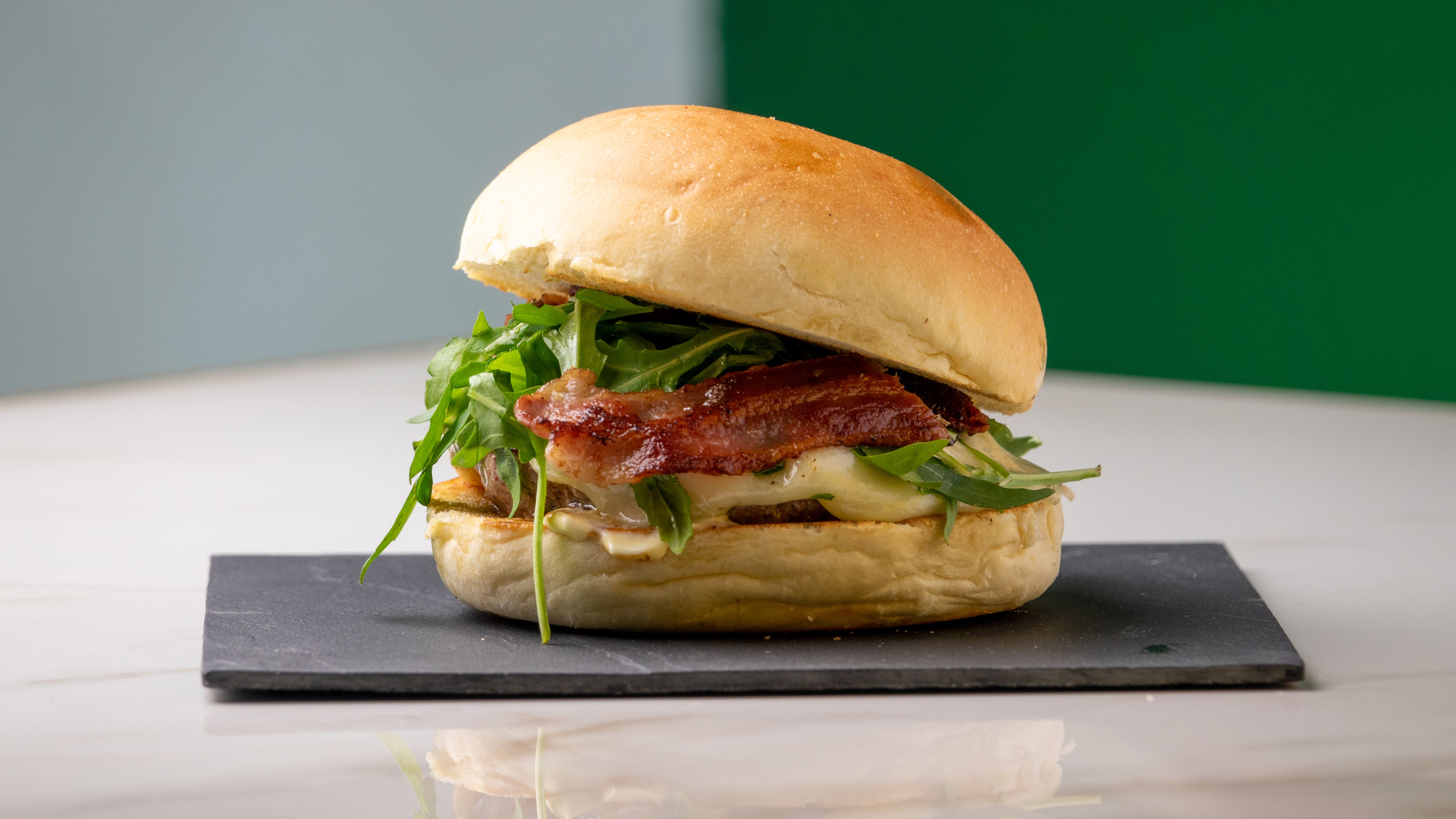 Bun con hamburger, rucola, formaggio e bacon servito da Symposium